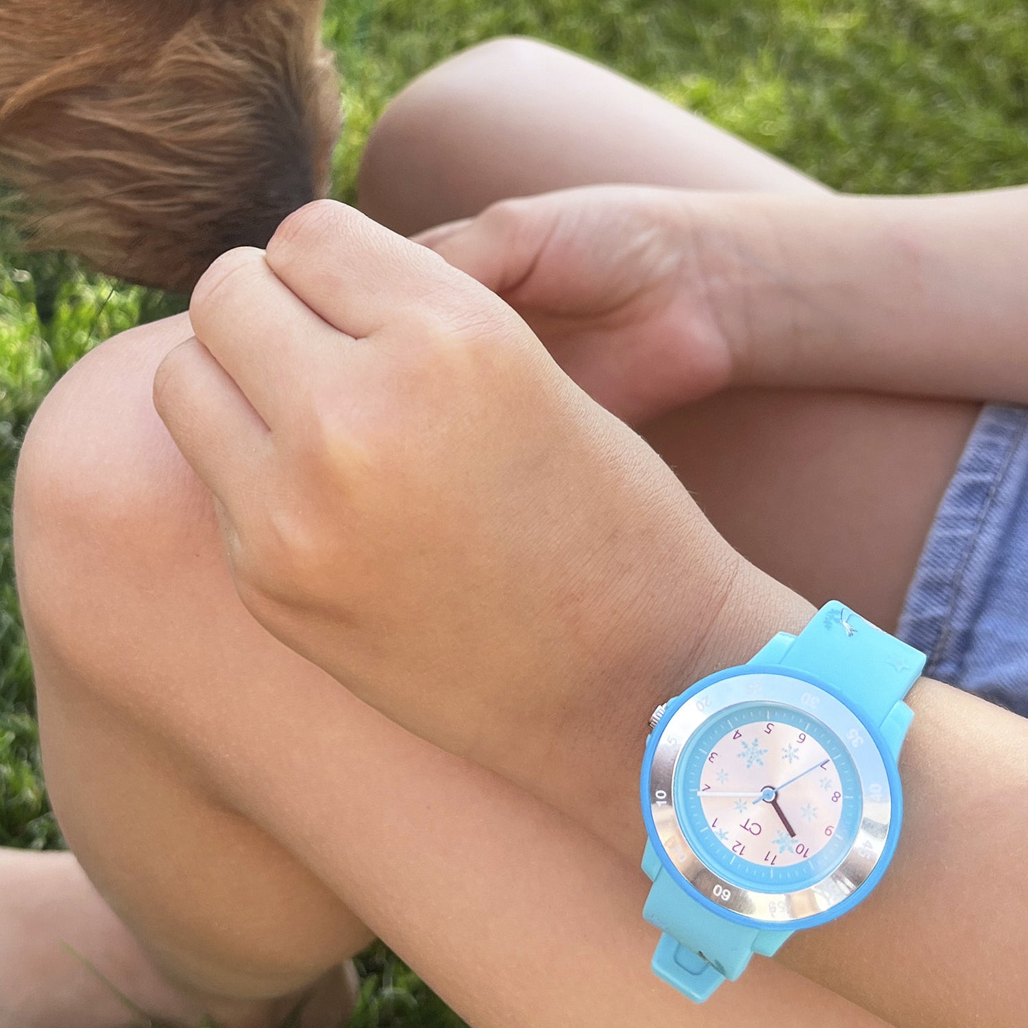 Ein Kind, das eine Cool Time Kids Armbanduhr - The Cool Ice Princess von Cool Time trägt, sitzt im Gras und streichelt einen braunen Hund mit angezogenen Knien.