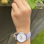Eine Kinderhand, die eine Cool Time Kids Armbanduhr - The Cool Lilac Rainbow trägt, streckt sich nach reifenden Erdbeeren an einer Gartenmauer.