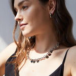 Frau mit gewelltem braunem Haar, trägt eine silberne Halskette und Echtzeit Creole - The Modern Basic von Echtzeit, gepaart mit einem schwarzen Oberteil - ein modernes Accessoire, das nach links schaut.