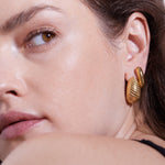 Nahaufnahme des Gesichts einer Frau, die Echtzeit Creole - The Organic Drop von Echtzeit trägt, einen goldenen Ohrring in Muschelform, der dieses elegante Damen Accessoire hervorhebt.