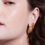 Nahaufnahme eines Frauengesichts, das den Echtzeit Creole - The Organic Drop trägt, einen großen, goldenen, strukturierten Creolenohrring von Echtzeit-einem eleganten Damen Accessoire.