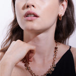 Eine Frau trägt die Echtzeit Creole - The Modern Basic Ohrringe und eine goldene Herzkette mit einem schwarzen ärmellosen Oberteil und schaut zur Seite - stilvolles Echtzeit-Accessoire mit modernem Design für Frauen.