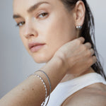 Frau mit nassen Haaren und natürlichem Make-up trägt das Echtzeit Armband - The Sleek One und silberne Ohrringe von Echtzeit, gestylt mit einem weißen Oberteil.