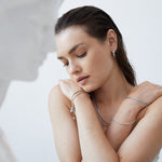 Eine Frau mit geschlossenen Augen posiert mit verschränkten Armen, trägt silbernen Echtzeit Schmuck und das filigrane Echtzeit Armband - Like Diamonds; im Vordergrund erscheint eine weiße Statue.