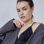 Eine Frau mit grauem Blazer und schwarzem Oberteil trägt die Echtzeit Halskette - Like Diamonds von Echtzeit, eine zeitlose, mehrlagige Halskette mit Tropfenanhänger, und schaut selbstbewusst in die Kamera.