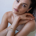 Hellhäutige Frau mit braunem Haar stützt ihr Kinn auf die Hände. Sie trägt das Echtzeit Armband - Like Diamonds von Echtzeit und mehrschichtige Armbänder.