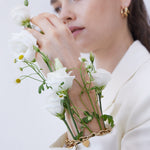 Eine Frau in einem weißen Blazer trägt weiße Blumen und Grünzeug auf ihrer Hand und ihrem Handgelenk, gepaart mit dem Echtzeit Armband - Endless Love von Echtzeit.