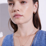 Frau trägt ein Denim-Oberteil, Echtzeit Halskette - Puffy Heart von Echtzeit, und dazu passende goldene herzförmige Ohrringe - ein zeitloses Accessoire für jeden Anlass.