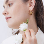 Frau mit goldenen Creolen und weißen Blüten in der Hand – zarter, natürlicher Look mit elegantem Schmuck-Statement.