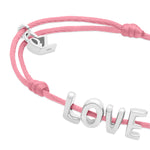 Das Echtzeit Armband - Love Letters von Echtzeit ist ein pinkes Stoffband mit silbernen LOVE-Buchstabenanhänger und kleinem silbernen Charm.