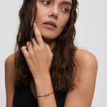Echtzeit Armband Love Letters – filigranes rotes Kordelarmband mit goldenem LOVE-Schriftzug, getragen am Handgelenk