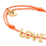 Das Echtzeit Armband - Love Letters der Marke Echtzeit ist ein orangefarbenes Stoffband mit goldenen LOVE-Buchstabenanhängern und einem kleinen goldenen Charm - ein stilvoller Akzent für jedes Outfit.