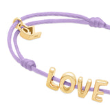 Das Echtzeit Armband - Love Letters von Echtzeit besteht aus einem lilafarbenen Stoffband mit einem goldenen LOVE Letter Charm und einem kleinen goldenen Boot - perfekt als einzigartiges Geschenk.