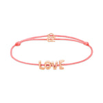 Das Echtzeit Armband - Love Letters von Echtzeit mit LOVE-Buchstabenanhänger und goldfarbenem Verschluss ist ein stilvolles Geschenk auf weißem Hintergrund.