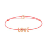 Das Echtzeit Armband - Love Letters von Echtzeit mit LOVE-Buchstabenanhänger und goldfarbenem Verschluss ist ein stilvolles Geschenk auf weißem Hintergrund.