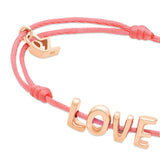 Das Echtzeit Armband - Love Letters von Echtzeit besteht aus einer rosafarbenen Kordel mit goldenen LOVE-Buchstaben und einem goldenen Herz - ein Geschenk, das von Herzen kommt.