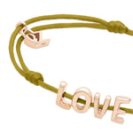 Das Echtzeit Armband - Love Letters von Echtzeit besteht aus einem olivgrünen Band mit goldenen LOVE Buchstaben und einem kleinen goldenen Akzent - ein ideales Geschenk für einen besonderen Menschen.