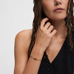 Frau mit nassen Haaren und schwarzem ärmellosen Oberteil trägt das Echtzeit Armband - Love Letters von Echtzeit, ein zartes goldenes Accessoire - ideal als Geschenk oder in Kombination mit Ihrem Lieblingsinitialanhänger.