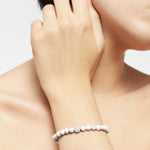 Eine Person, die das Armband LIEBESKIND BERLIN Beads - The Textured Howlith von Liebeskind Berlin trägt, stützt ihre Hand vor einem schlichten Hintergrund auf ihr Gesicht.