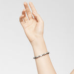 Eine mit Liebeskind Berlin Perlen geschmückte Hand - Das Armband Textured Jaspis erhebt sich vor einem schlichten, hellen Hintergrund und unterstreicht die subtile Eleganz des Liebeskind Berlin Schmucks.