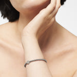 Eine Person stützt ihr Kinn auf ihre Hand und trägt das Liebeskind Berlin Beads - The Simple Steel Damenarmband am Handgelenk.
