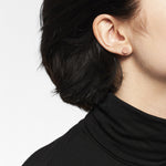 Nahaufnahme einer Person mit kurzen dunklen Haaren in einem schwarzen Rollkragenpullover, die den LIEBESKIND BERLIN Ohrstecker - The Iconic Geometric von Liebeskind Berlin trägt.