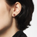 Nahaufnahme einer Person mit kurzen dunklen Haaren, die einen kleinen sechseckigen LIEBESKIND BERLIN Ohrstecker - The Iconic Geometric von Liebeskind Berlin in einem Ohr trägt.