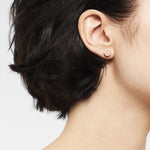 Nahaufnahme des Ohres einer Frau mit kurzen dunklen Haaren, die den LIEBESKIND BERLIN Ohrstecker - Keep Loving von Liebeskind Berlin für einen eleganten Ear Candy Style trägt.