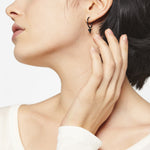Frau mit kurzen dunklen Haaren, die ihren Nacken berühren, trägt Liebeskind Berlin Creole - The Cone Ohrringe und ein sichtbares weißes Oberteil.
