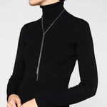 Eine Person mit schwarzem Rollkragen trägt die LIEBESKIND BERLIN Halskette - The Everyday Combination von Liebeskind Berlin, die mit ihrem langen silbernen Design einen modernen Akzent vor einem schlichten Hintergrund setzt.