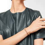 Eine Person in einem dunklen, kurzärmeligen Lederoberteil präsentiert das Liebeskind Berlin Beads - Pink Opal Armband, indem sie vor einem schlichten Hintergrund elegant den Arm über dem Körper kreuzt.