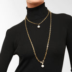 Eine Person mit schwarzem Rollkragen trägt zwei Liebeskind Berlin "The Long Pearl" Halsketten, Goldketten mit je einem einzelnen Perlenanhänger, perfekt gestylt als elegante Damen Gliederkette oder Perlenkette.