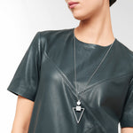 Eine Frau in einem dunkelgrünen Ledertop stylt ihren Look mit der LIEBESKIND BERLIN Halskette - The Geometric von Liebeskind Berlin, die mit ihren geometrischen Anhängern für einen schicken 70er-Jahre-Look sorgt.