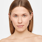 Eine Frau mit glattem, hellbraunem Haar trägt die Liebeskind Berlin Creole - Twisted Ohrringe und schaut in die Kamera vor einem schlichten Hintergrund.