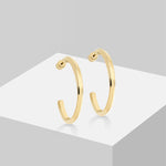 Die LIEBESKIND BERLIN Creole - Twisted aus Edelstahl von Liebeskind Berlin ist stilvoll auf einer weißen geometrischen Plattform vor grauem Hintergrund präsentiert.