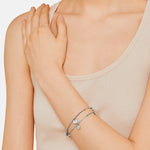 Eine Frau in einem beigen Tank-Top trägt das zarte LIEBESKIND BERLIN Armband - The Mirror von Liebeskind Berlin im Boho-Stil, die Hand ruht auf ihrer Schulter.
