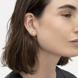 Eine Frau mit kurzen braunen Haaren im Profil trägt ein schwarzes Oberteil und das LIEBESKIND BERLIN Set - Sparkling Rosé von Liebeskind Berlin mit kleinen, runden roségoldenen Ohrsteckern.