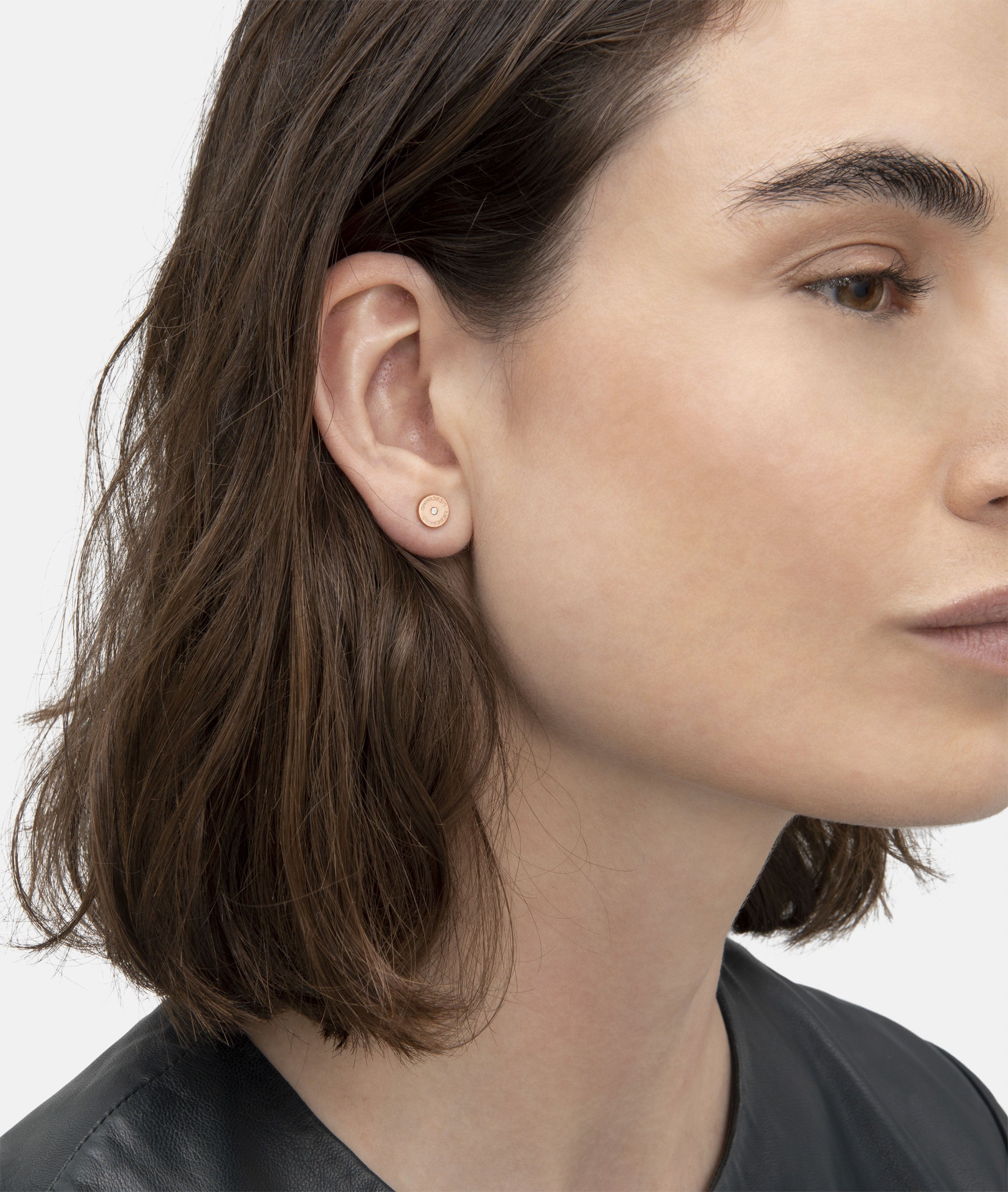 Eine Frau mit kurzen braunen Haaren im Profil trägt ein schwarzes Oberteil und das LIEBESKIND BERLIN Set - Sparkling Rosé von Liebeskind Berlin mit kleinen, runden roségoldenen Ohrsteckern.