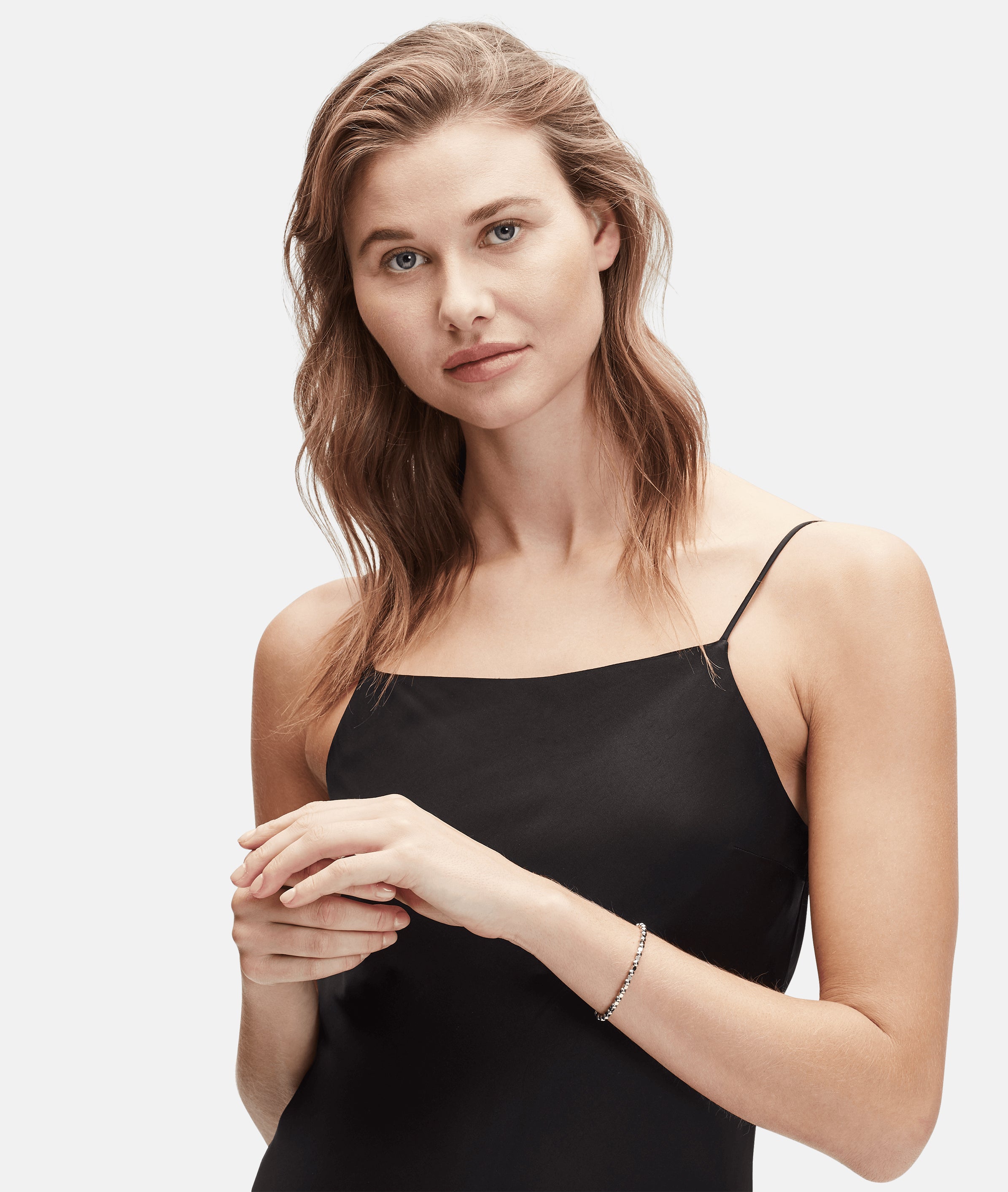 Frau mit gewelltem hellbraunem Haar, die ein schwarzes ärmelloses Kleid, ein Beads-Armband und das Liebeskind Berlin Set - Silver Berry Everyday trägt, posiert vor einem schlichten Hintergrund.