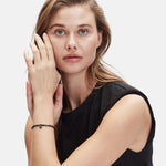 Eine Frau mit langen Haaren in einem ärmellosen schwarzen Oberteil berührt ihr Gesicht, trägt ein zartes Armband und das Liebeskind Berlin Set - Black Urban von Liebeskind Berlin.