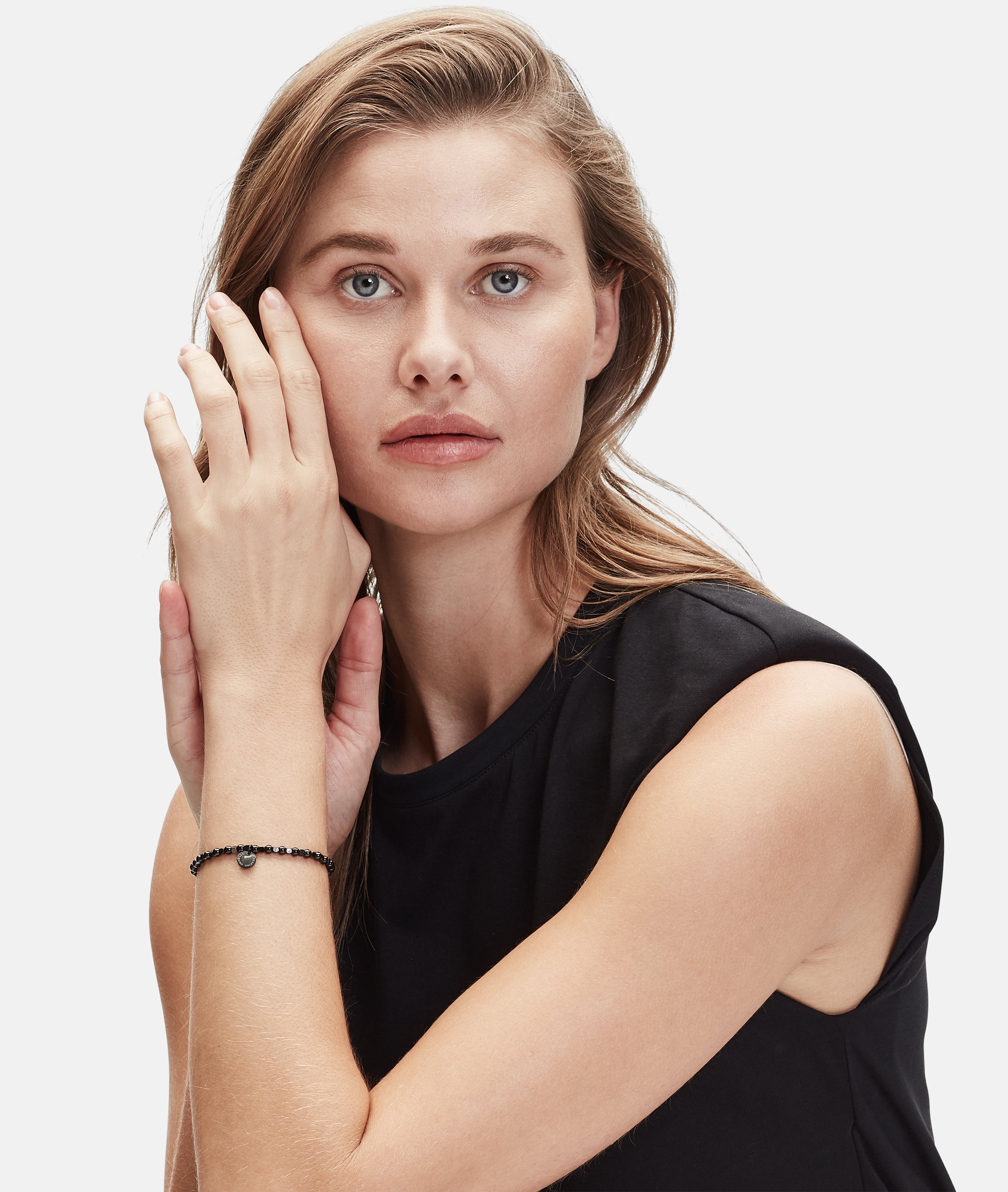 Eine Frau mit langen Haaren in einem ärmellosen schwarzen Oberteil berührt ihr Gesicht, trägt ein zartes Armband und das Liebeskind Berlin Set - Black Urban von Liebeskind Berlin.