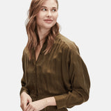Frau mit gewelltem braunem Haar und olivgrüner Bluse, zur Seite lächelnd, mit einer goldenen Uhr und dem Liebeskind Berlin Gold Everyday Layering Set ausgestattet.