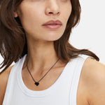 Eine Frau in einem weißen Tank-Top trägt die schwarze Liebeskind Berlin Classy Heart Halskette, die ihrem Look einen modernen Touch verleiht.