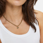 Frau trägt ein weißes Tank-Top und die LIEBESKIND BERLIN Halskette - Broken Heart Chunky von Liebeskind Berlin, die eine klobige Goldkette mit einem herzförmigen Anhänger aufweist.