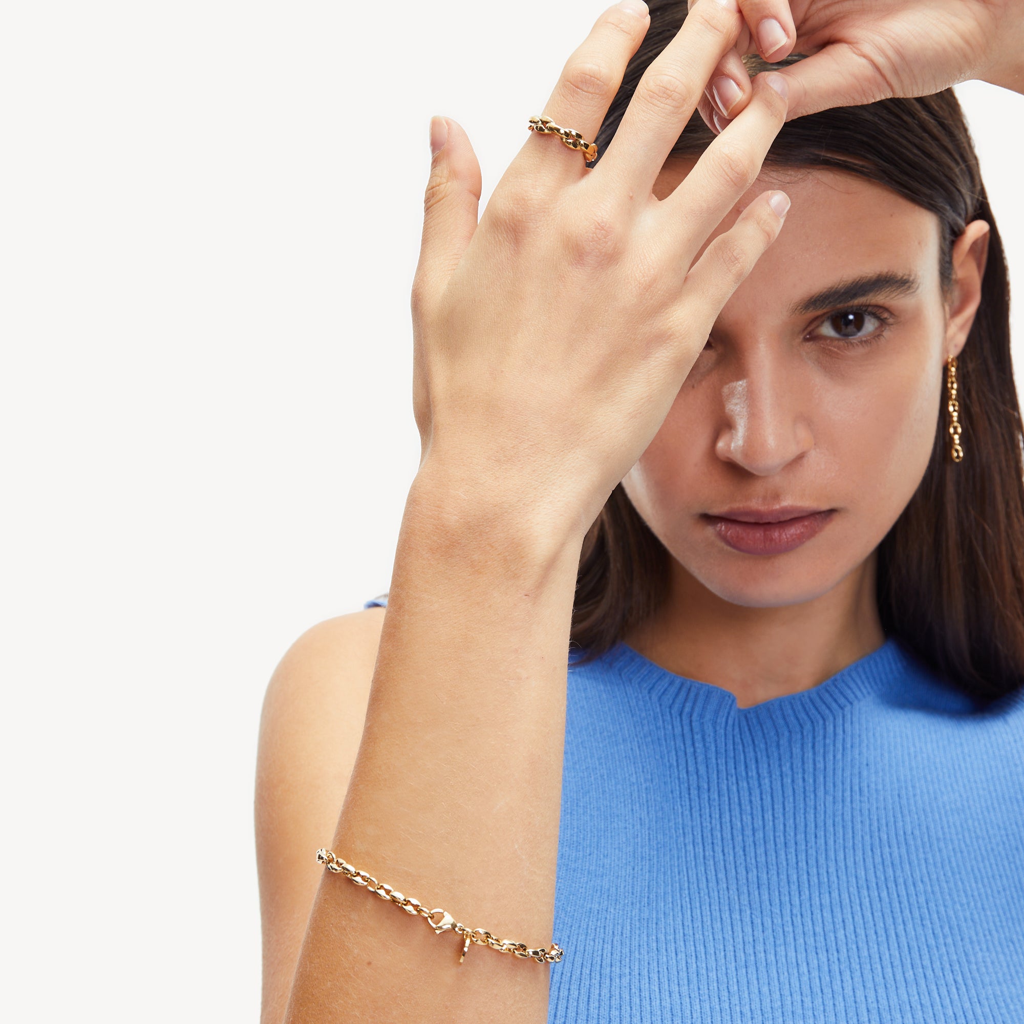 Frau in blauem Top posiert mit erhobener Hand und präsentiert Goldschmuck und das stilvolle Liebeskind Berlin Set - Gold Chic. Ihre Accessoires werden durch diese elegante goldfarbene Uhr von Liebeskind Berlin ergänzt.