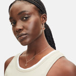 Eine Frau mit geflochtenen Haaren trägt geometrische goldene Ohrringe und die LIEBESKIND BERLIN Halskette - Swinging Icon von Liebeskind Berlin, gepaart mit einem leichten Tanktop für einen mühelos eleganten Look.