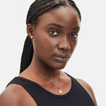 Frau mit geflochtenem Haar in einem schwarzen Tank-Top, trägt eine Anhänger-Halskette und Liebeskind Berlin LIEBESKIND BERLIN Ohrstecker - Loving Icon, looking forward.