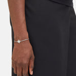 Eine Person in schwarzer Kleidung trägt ein zartes Liebeskind Berlin Armband - Swinging Icon mit einem kleinen quadratischen Logomania-Anhänger an ihrem Handgelenk.