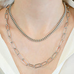 Das LIEBESKIND BERLIN Halsketten-Set - The Layering von Liebeskind Berlin besteht aus zwei silbernen Ketten, darunter eine klobige und eine mit großen Gliedern, die stilvoll über ein weißes Shirt gelegt werden.