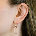 Nahaufnahme eines Frauenohrs mit LIEBESKIND BERLIN Ohrhänger - Das Must-Have von Liebeskind Berlin: goldene geometrische Ohrhänger mit zwei miteinander verbundenen Ovalen, die Berliner Flair und elegantes Design versprühen.